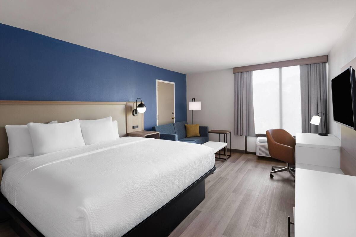 A hotel room with a large bed, a desk, a chair, a TV, and a window with curtains.