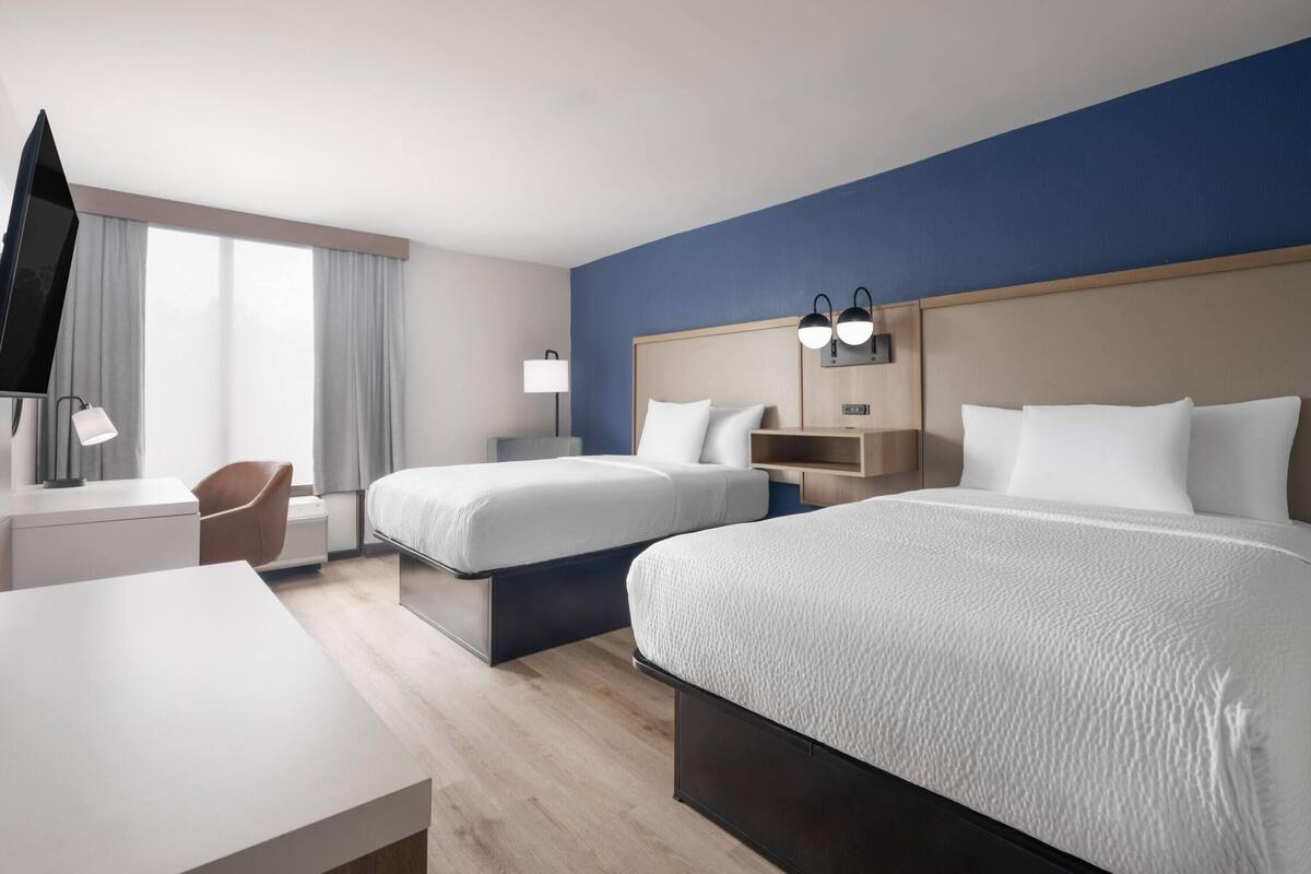 A hotel room with two beds, a desk, a chair, a TV, and a window with curtains.