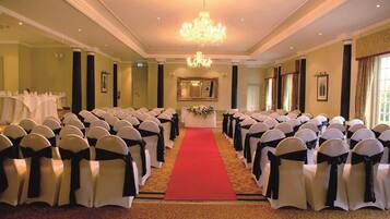 A formal event space with rows of white chairs with black sashes, a red carpet aisle, and a chandelier.