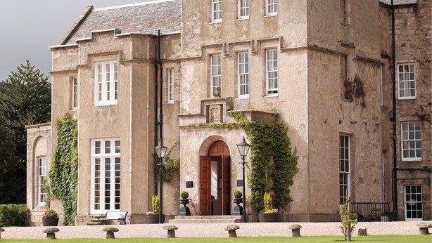 A large, historic building with a central tower, multiple windows, and a well-maintained lawn with stone benches. - Macdonald Pittodrie House (Inverurie)