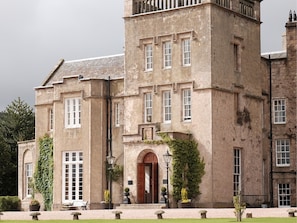 A large, historic building with a central tower, multiple windows, and a well-maintained lawn with stone benches. - Macdonald Pittodrie House (Inverurie)
