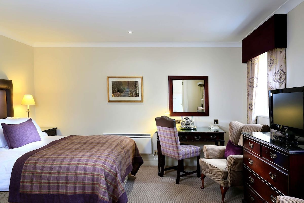 A hotel room with two beds, a desk with a chair, a television, a dresser, and a mirror.