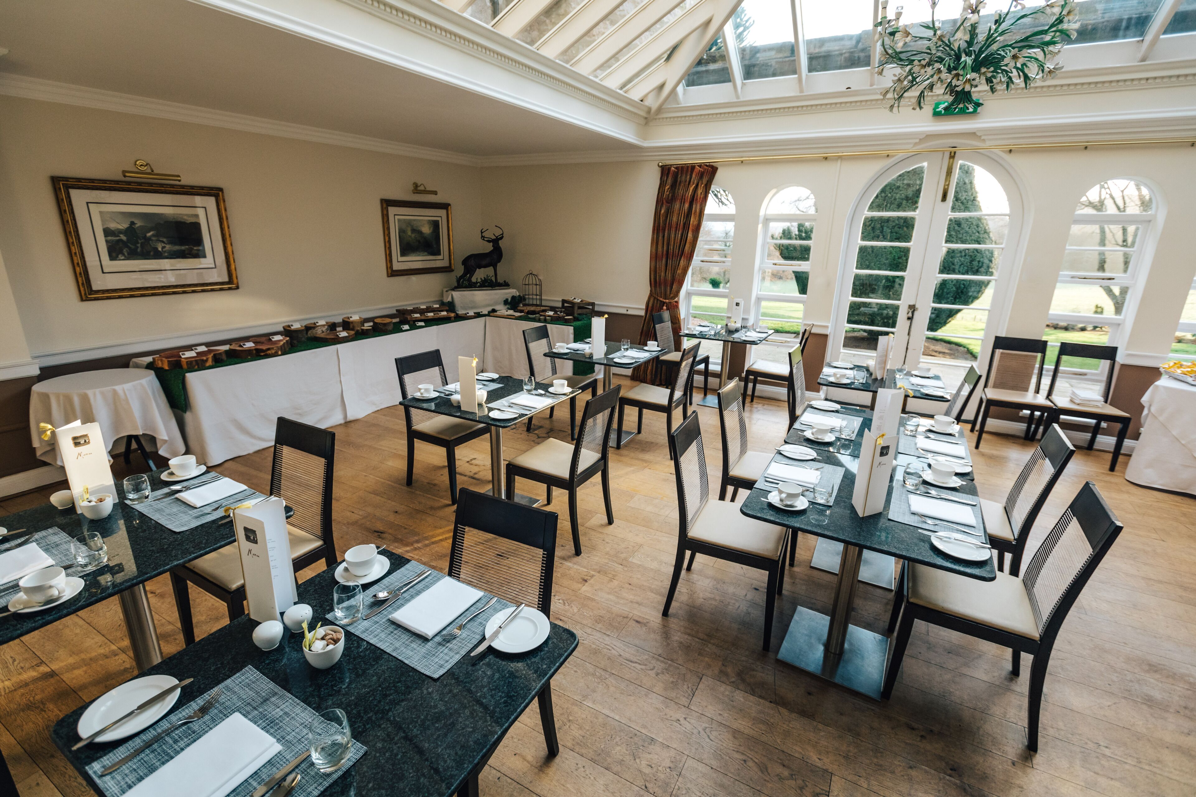Un espace repas avec des tables dressées pour le service, un bar et de grandes fenêtres offrant une vue sur l’extérieur.