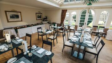 A dining area with tables set for service, a bar area, and large windows offering a view of the outdoors.