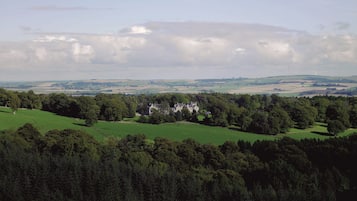 Un vaste domaine comprenant de grandes prairies verdoyantes et une imposante demeure entourée d’une forêt dense.