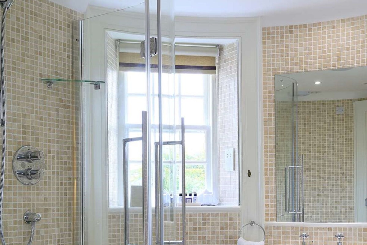 A bathroom with a glass-enclosed shower, a sink, and a window.