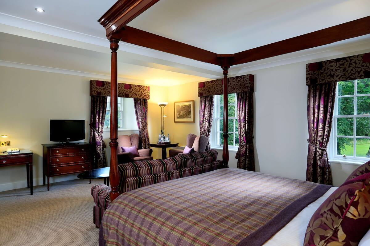 A bedroom with a four-poster bed, a television, a desk, and a chair.