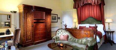 Un dormitorio tradicional con cama con dosel, un sillón verde, un armario de madera y una mesita redonda con bandeja.