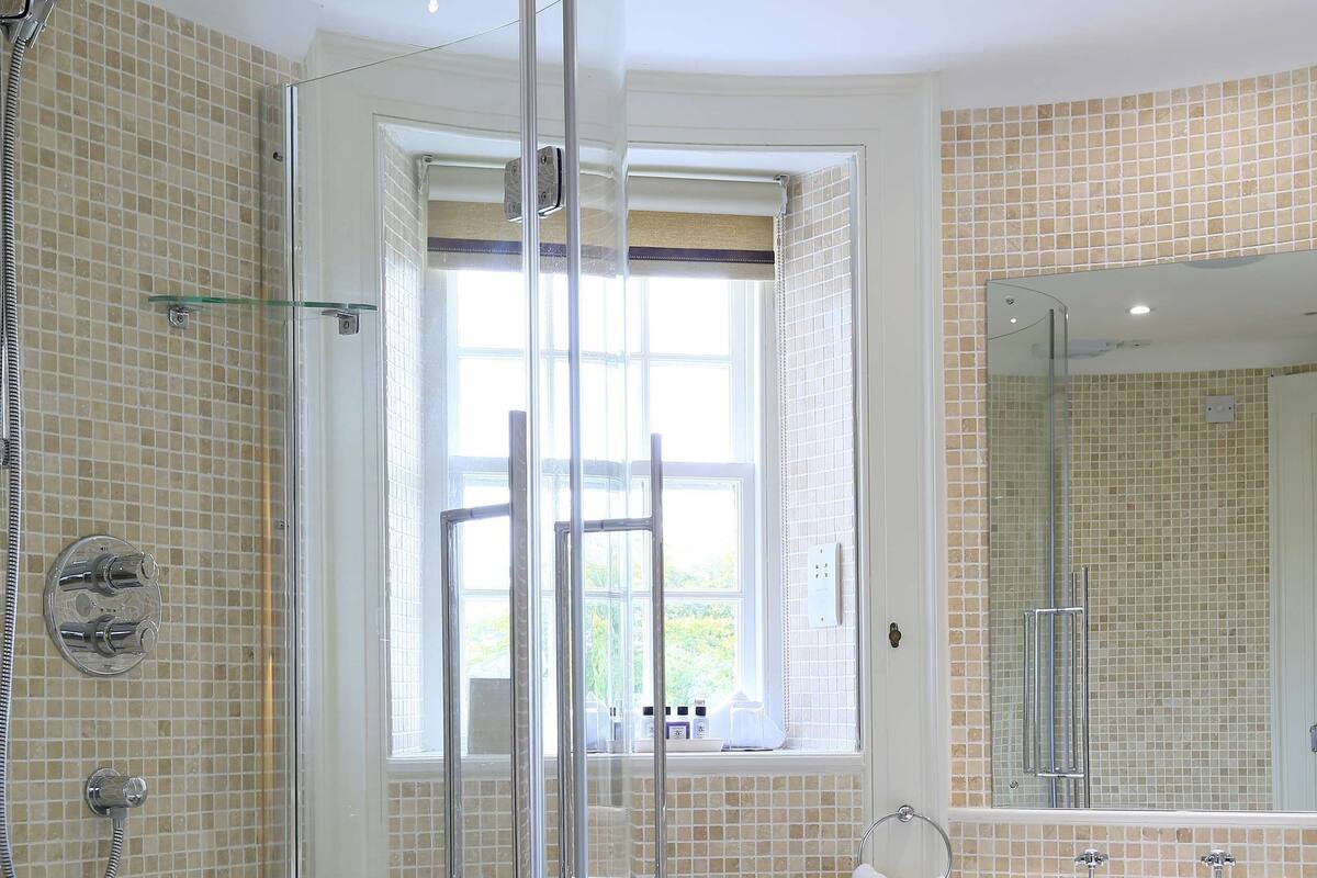 A bathroom with a glass-enclosed shower, a sink, and a window.
