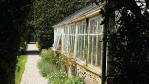 A greenhouse with a gravel path leading to it, surrounded by lush greenery and flowering plants. - Macdonald Pittodrie House (Inverurie)