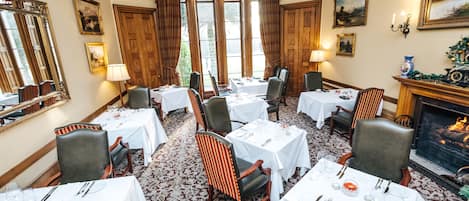 A dining room with multiple tables set for a meal, chairs, a fireplace, and framed artwork on the walls.