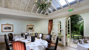 A dining room with a high ceiling, a chandelier, and a view of the garden through an open archway. - Macdonald Pittodrie House (Inverurie)