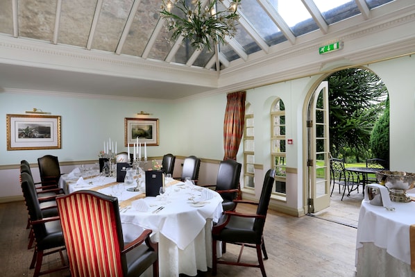 A dining room with a high ceiling, a chandelier, and a view of the garden through an open archway. - Macdonald Pittodrie House (Inverurie)
