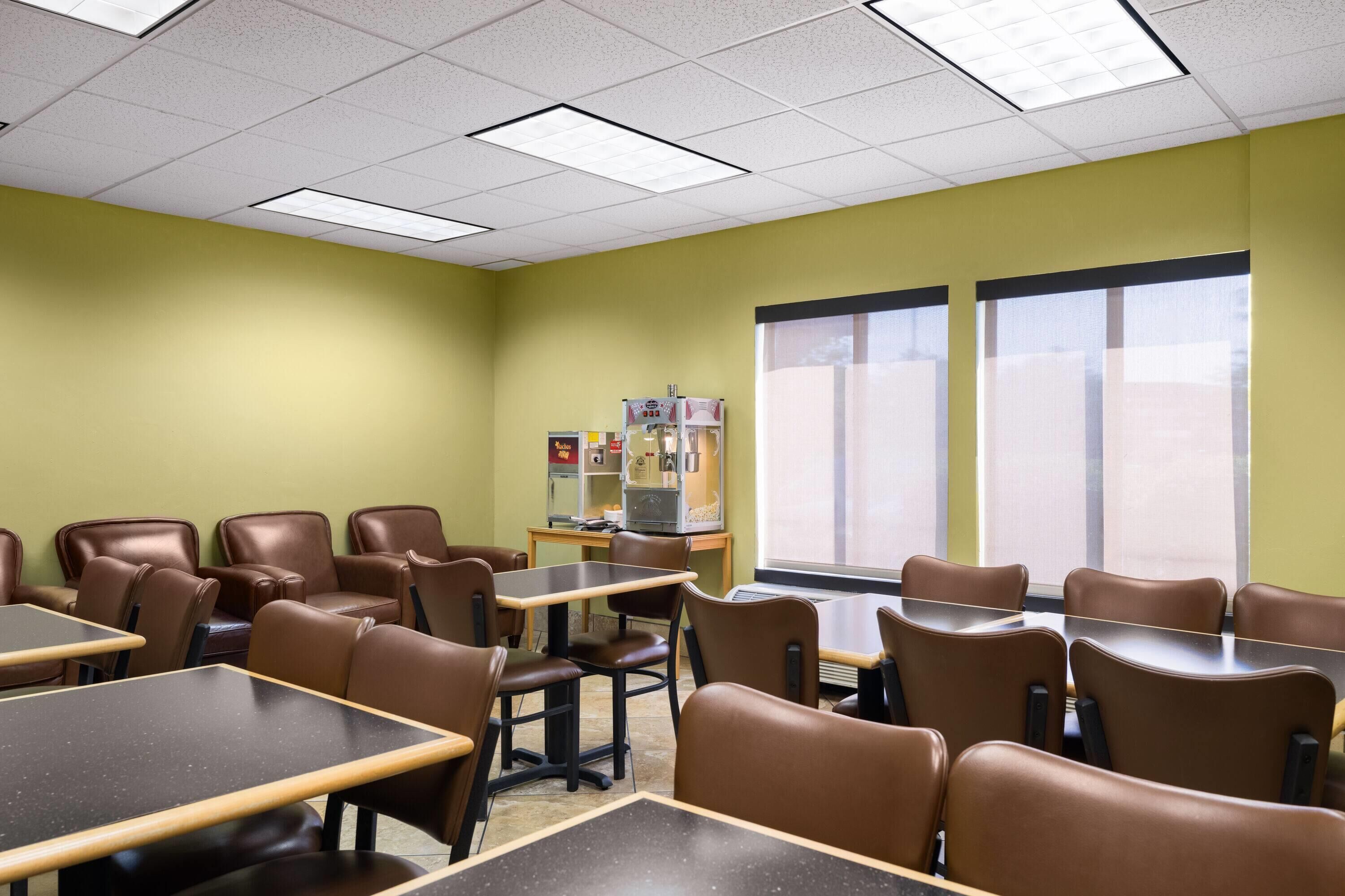 A conference room with tables and chairs, a window with blinds, and a vending machine.