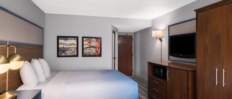 A hotel room with two beds, a TV, a desk with a lamp, and artwork on the wall.
