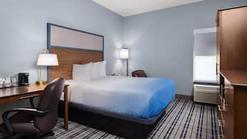 A hotel room with a bed, desk, chair, lamp, and air conditioning unit.