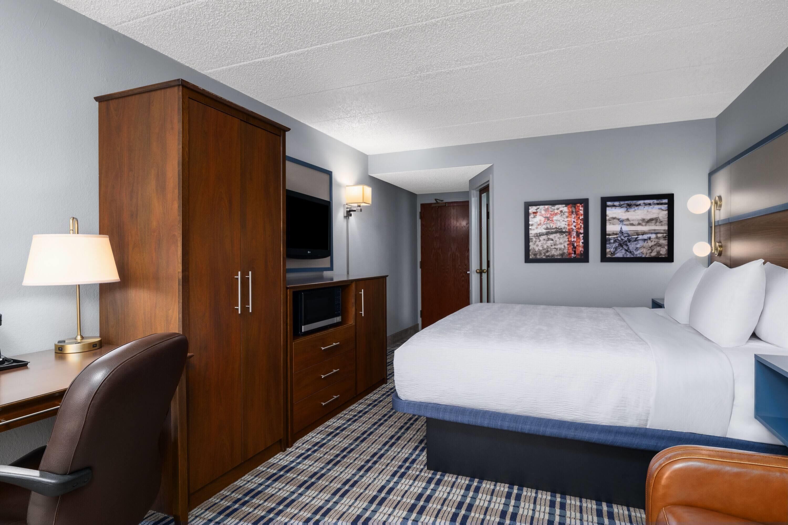Ein Hotelzimmer mit Bett, Schreibtisch, Fernseher, Kleiderschrank und Bildern an der Wand.