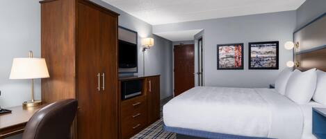 Une chambre d’hôtel équipée d’un lit, d’un bureau, d’une télévision, d’une armoire et d’œuvres d’art accrochées au mur.