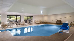 An indoor swimming pool with clear views of the outdoors, a blue chair, and a wooden bench.
