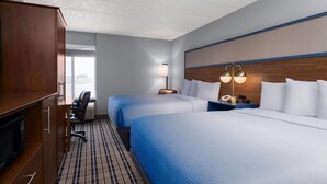 A hotel room with two beds, a desk, a chair, a wardrobe, and a lamp.