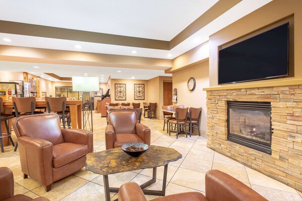 A spacious lobby with leather armchairs, a stone fireplace, and a flat-screen TV mounted above it. - AmericInn by Wyndham Madison West (Madison)