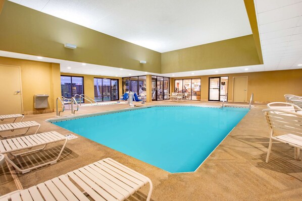 An indoor swimming pool with lounge chairs, a changing room, and a view of the outside. - AmericInn by Wyndham Madison West (Madison)