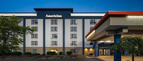 A hotel with a modern facade, a parking lot, and a well-lit entrance.