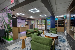 A modern lobby with green upholstered seating, a reception desk, a refrigerator, and a blue wall with shelves.