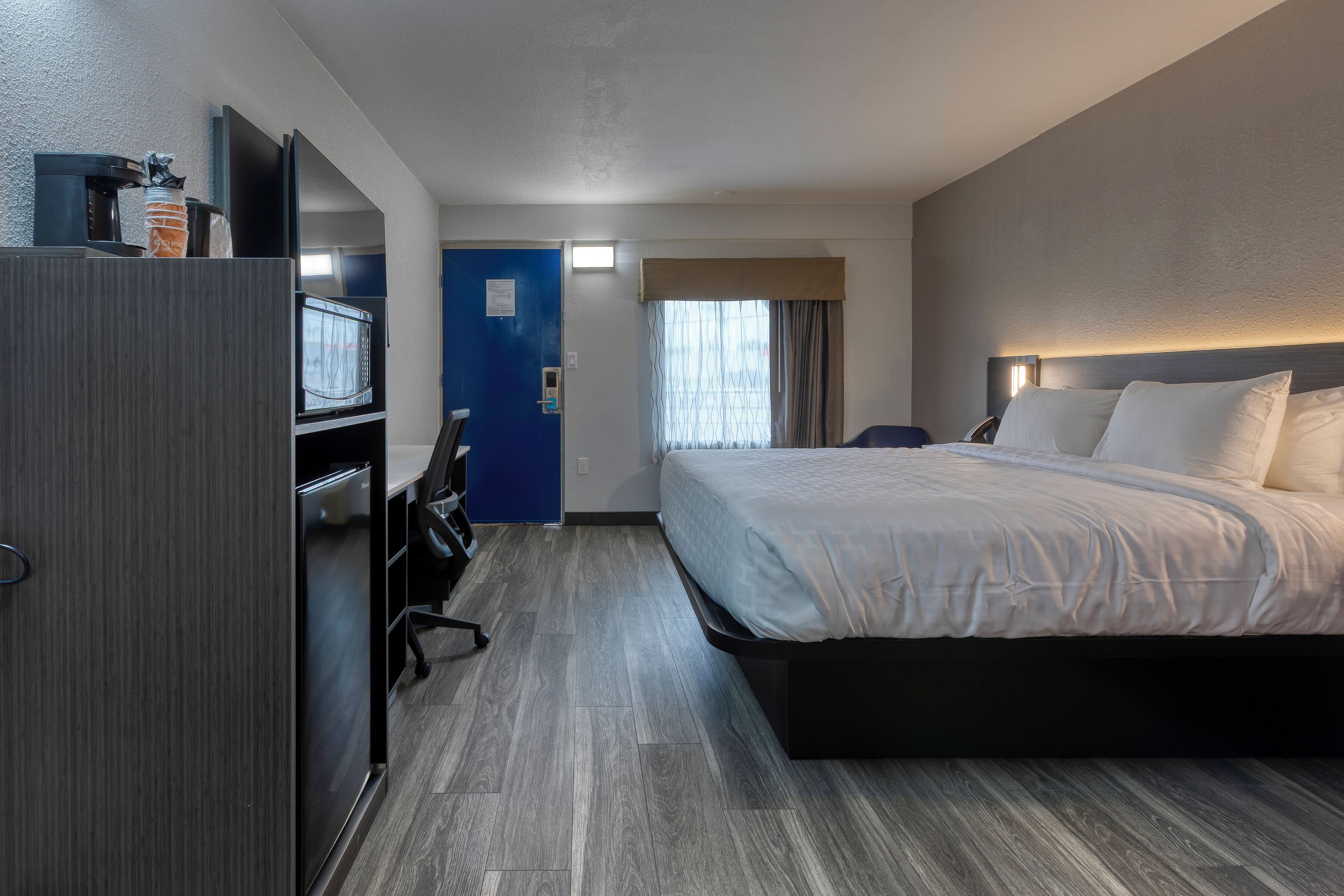 A hotel room with a bed, a desk with a computer, a TV, and a minibar.