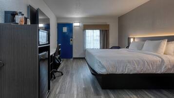 A hotel room with a bed, a desk with a computer, a TV, and a minibar.