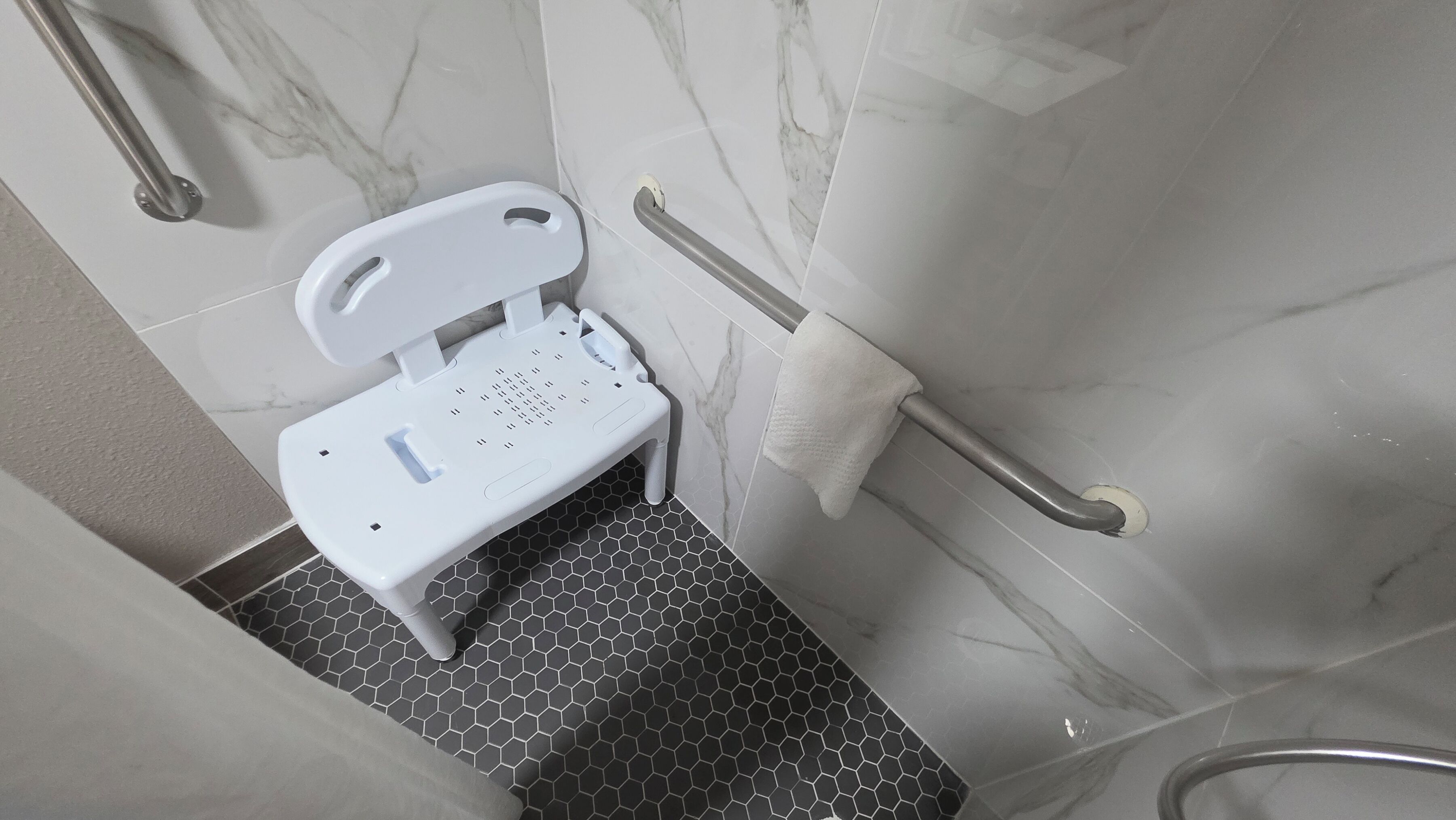 A bathroom with a white toilet, a handrail, a towel rack, and a hexagonal floor pattern.