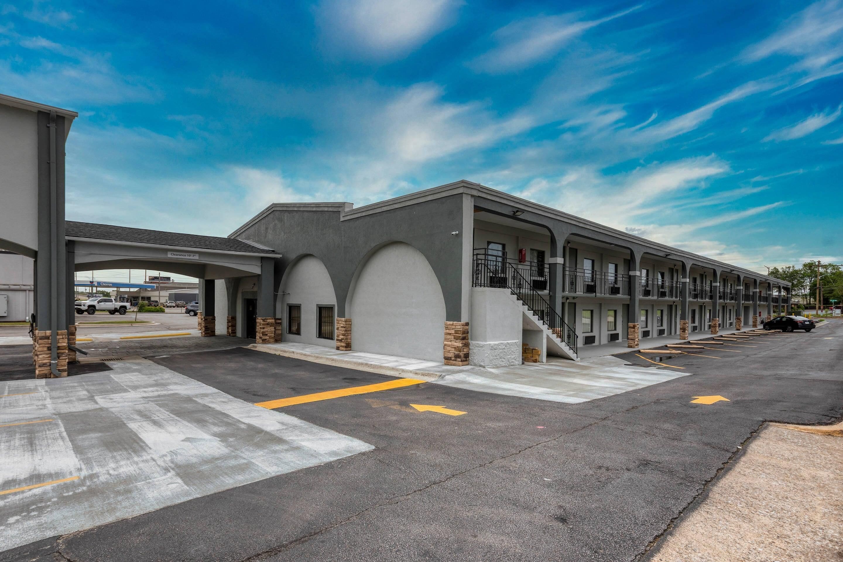 A motel with a row of rooms, a covered parking area, and a clear sky.
