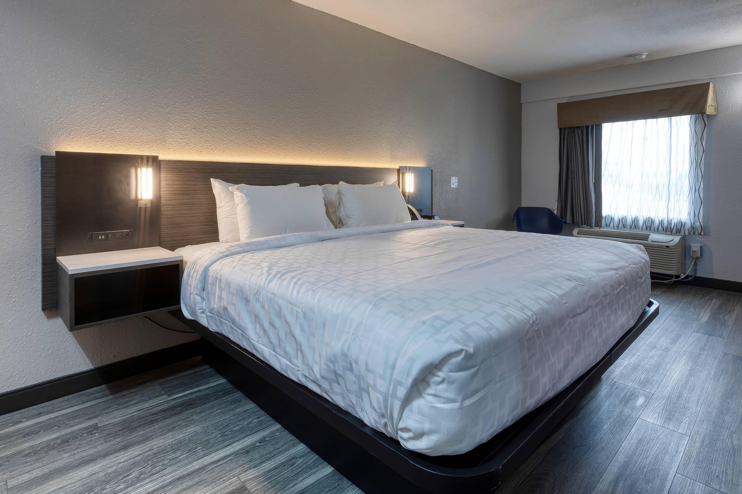 A hotel room with a large bed, bedside tables, a desk, and a window with curtains.