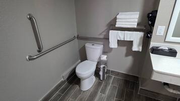 Une petite salle de bain moderne avec des toilettes blanches, une barre d’appui, un porte-serviettes et un lavabo avec un miroir.