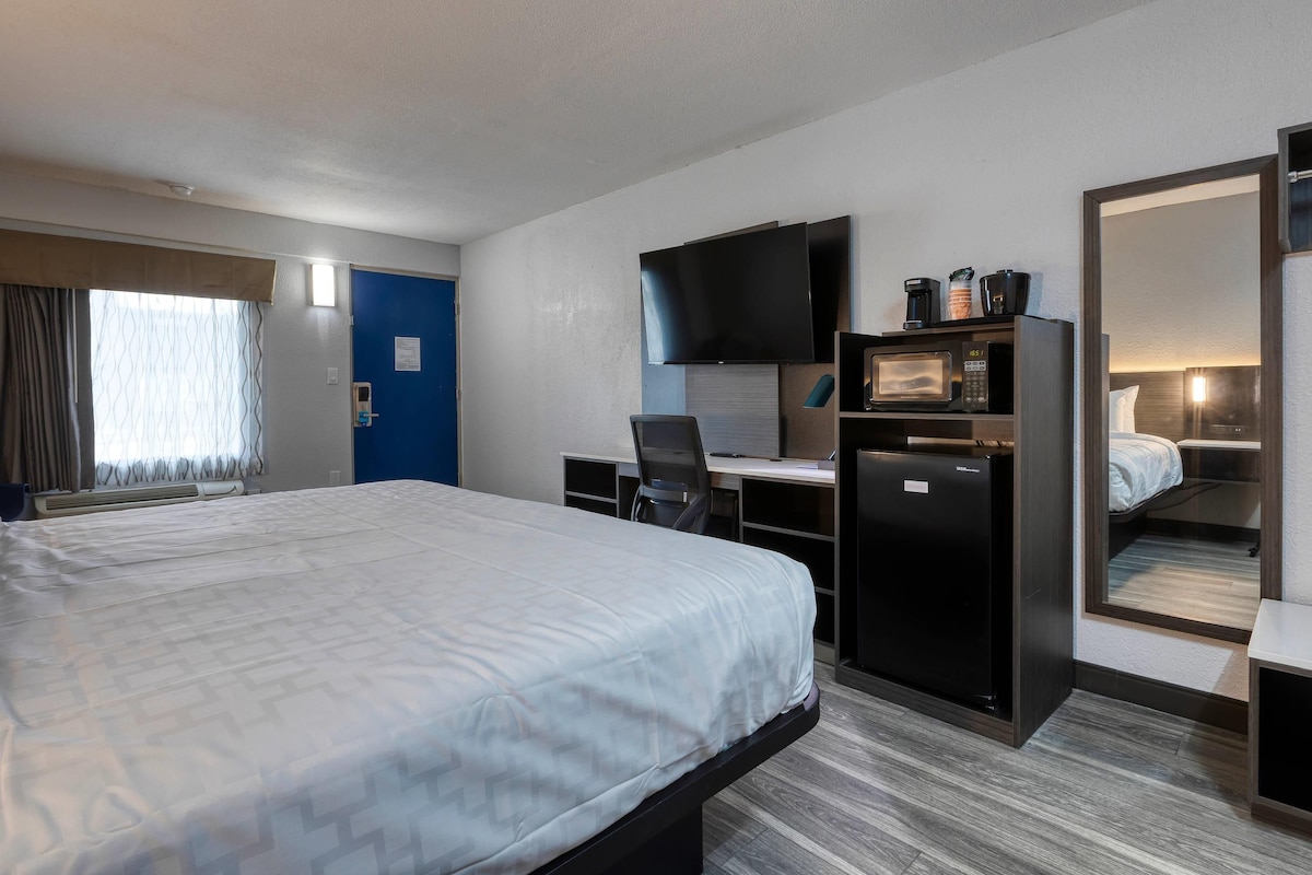 A hotel room with a bed, a desk with a computer, a television, and a microwave.