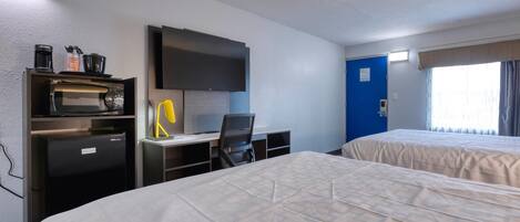 A hotel room with a bed, a desk with a chair, a microwave, a refrigerator, a television, and a window with curtains.