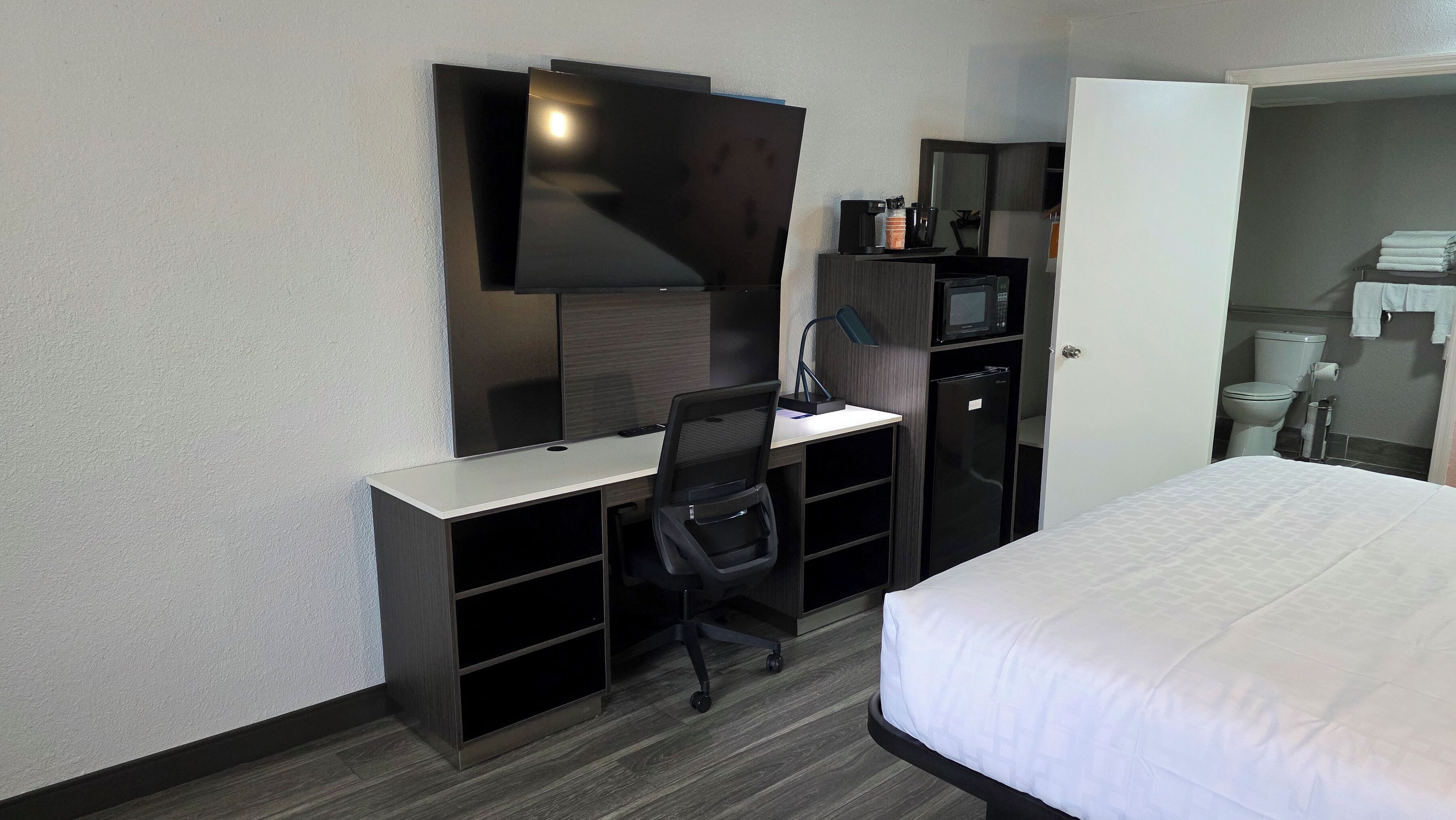 A hotel room with a bed, a desk with a chair, a television, a microwave, and a refrigerator.