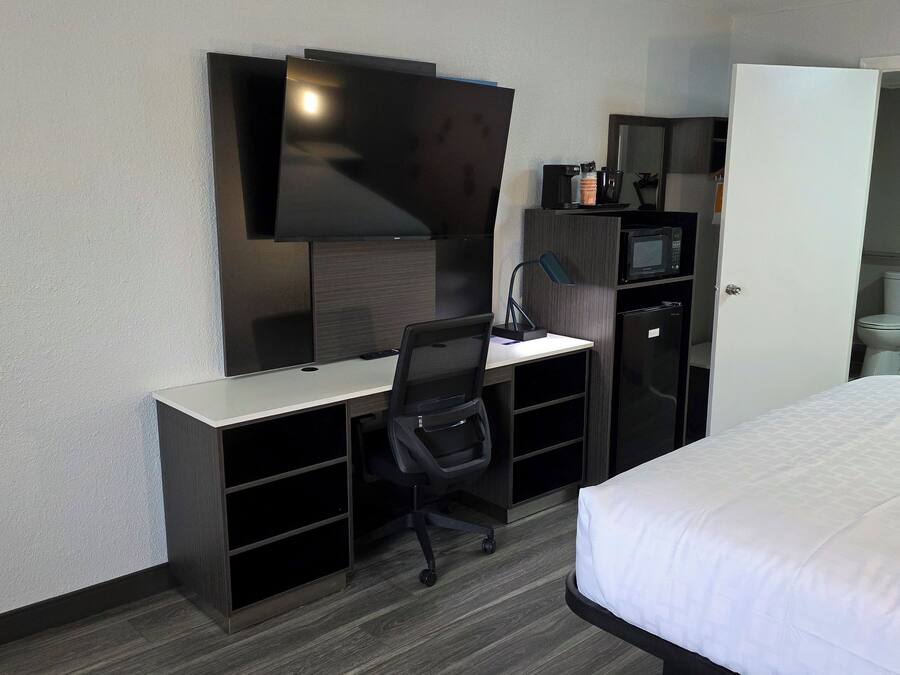 A hotel room with a bed, a desk with a chair, a television, a microwave, and a refrigerator.