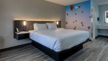 A modern hotel room with a large bed, a bedside table with a lamp, and a wall with a mural of hot air balloons.