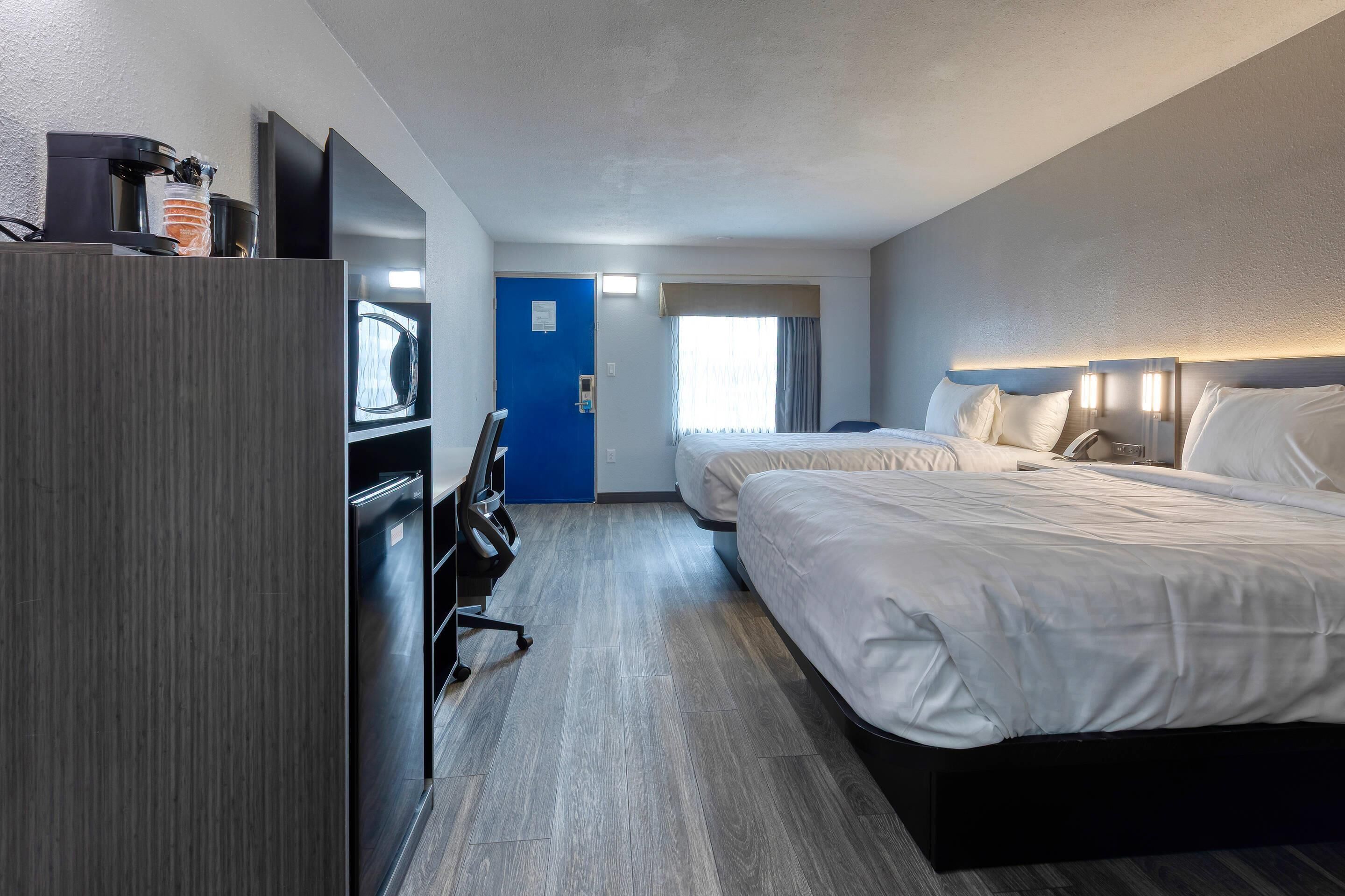 Ein Hotelzimmer mit Schreibtisch, zwei Betten, einem Fernseher und einer Tür.