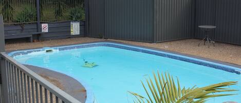Una piscina rectangular con borde de azulejos, rodeada por una valla metálica y una pequeña mesa.