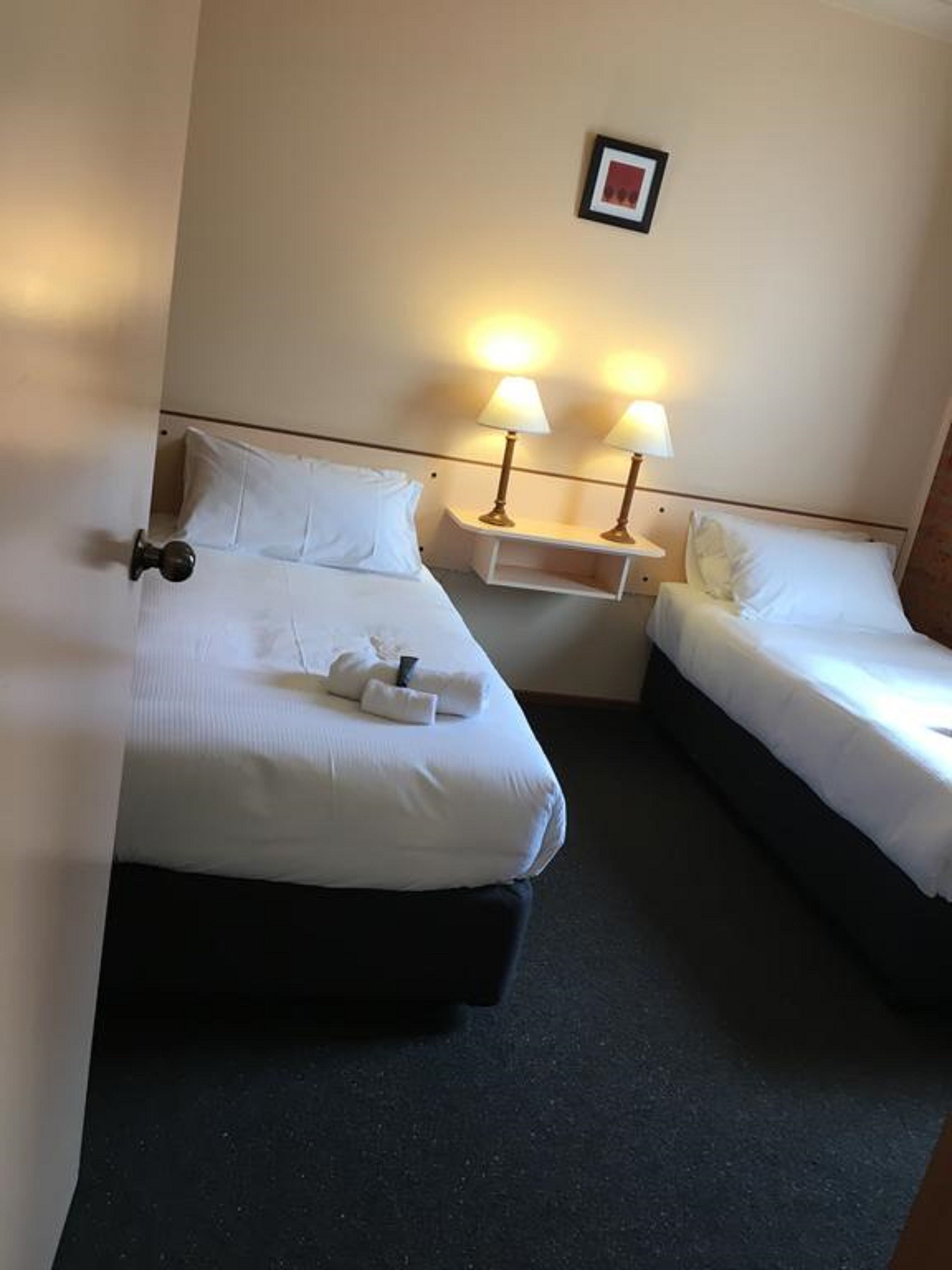 Une chambre d’hôtel avec deux lits, une table de chevet avec des lampes et un tableau encadré au mur.