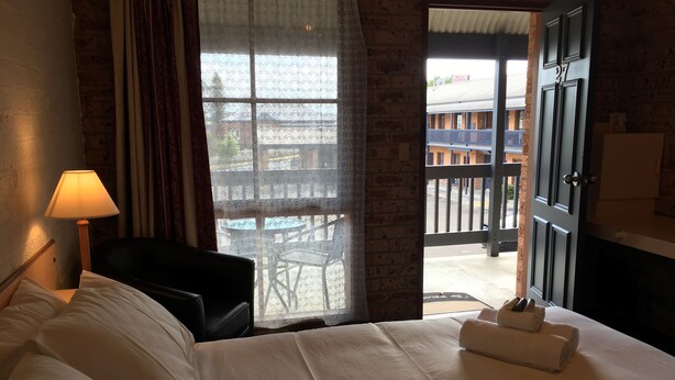 A hotel room with a bed, a desk, a lamp, a window with a view of the outside, and a door leading to a balcony. - Bega Downs Motor Inn (Bega)