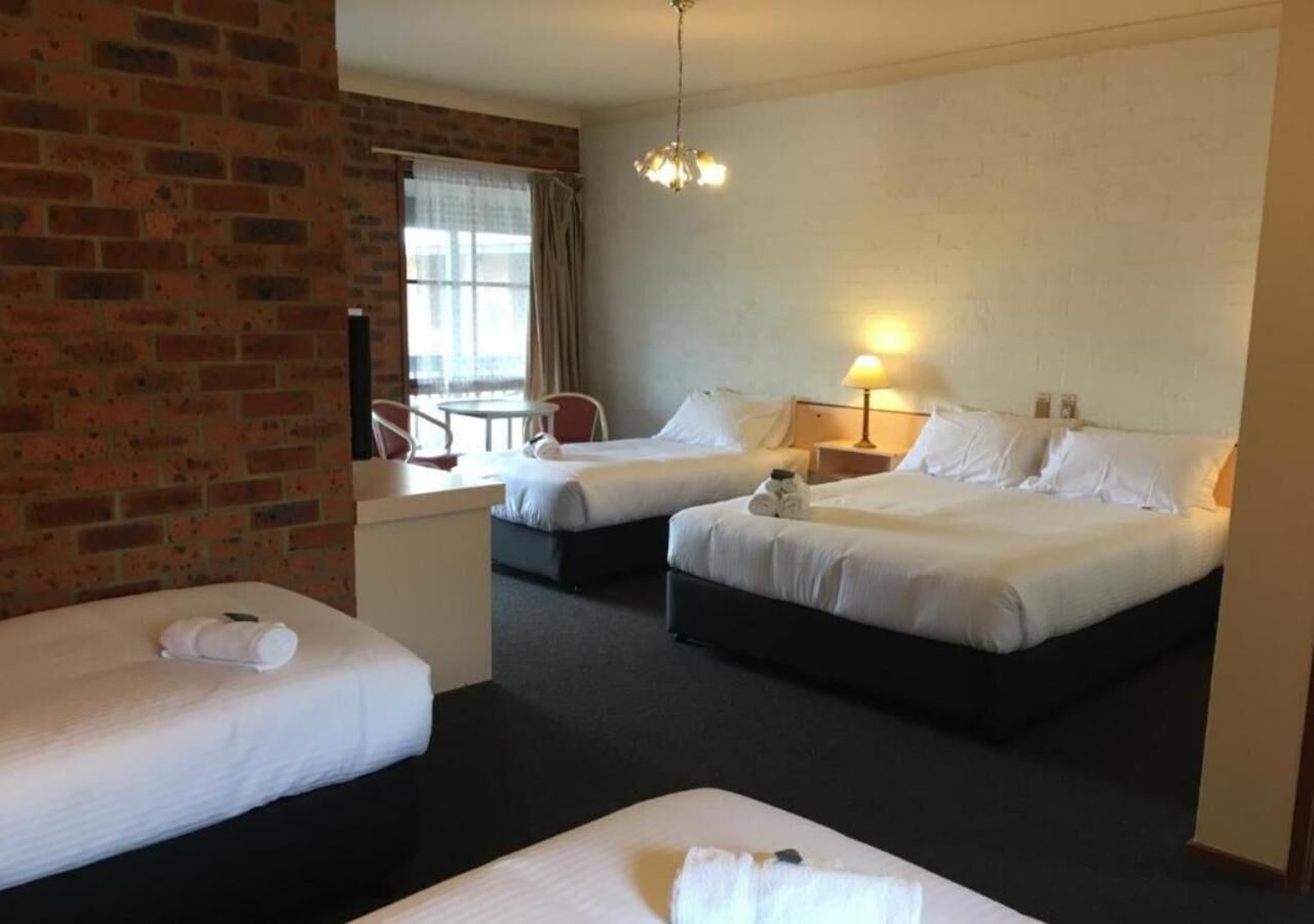 A hotel room with two beds, a small desk, a chair, and a window with curtains.