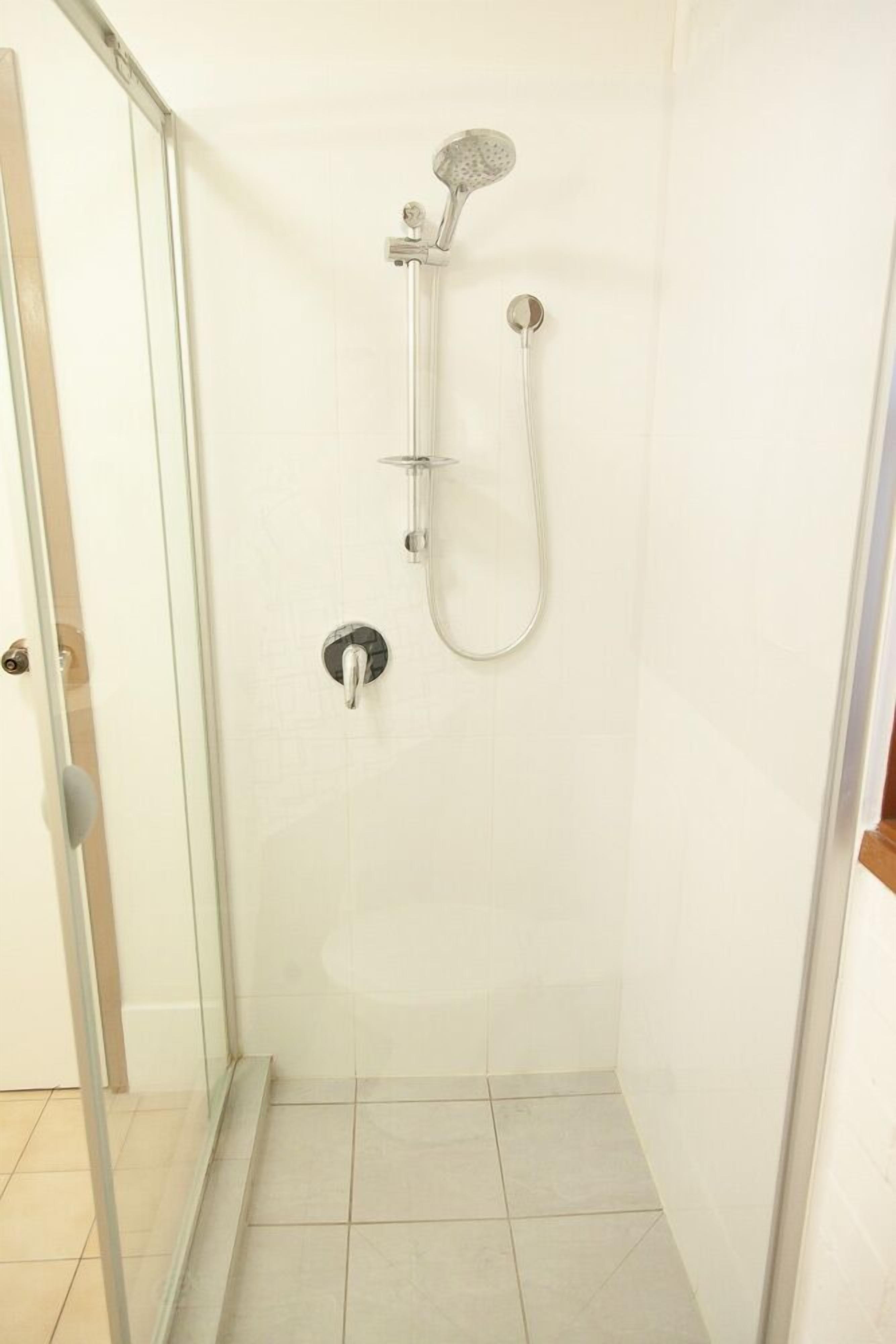 A shower with a handheld showerhead and a wall-mounted faucet in a tiled room.