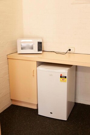 A small kitchenette with a microwave on a countertop and a mini-fridge below.