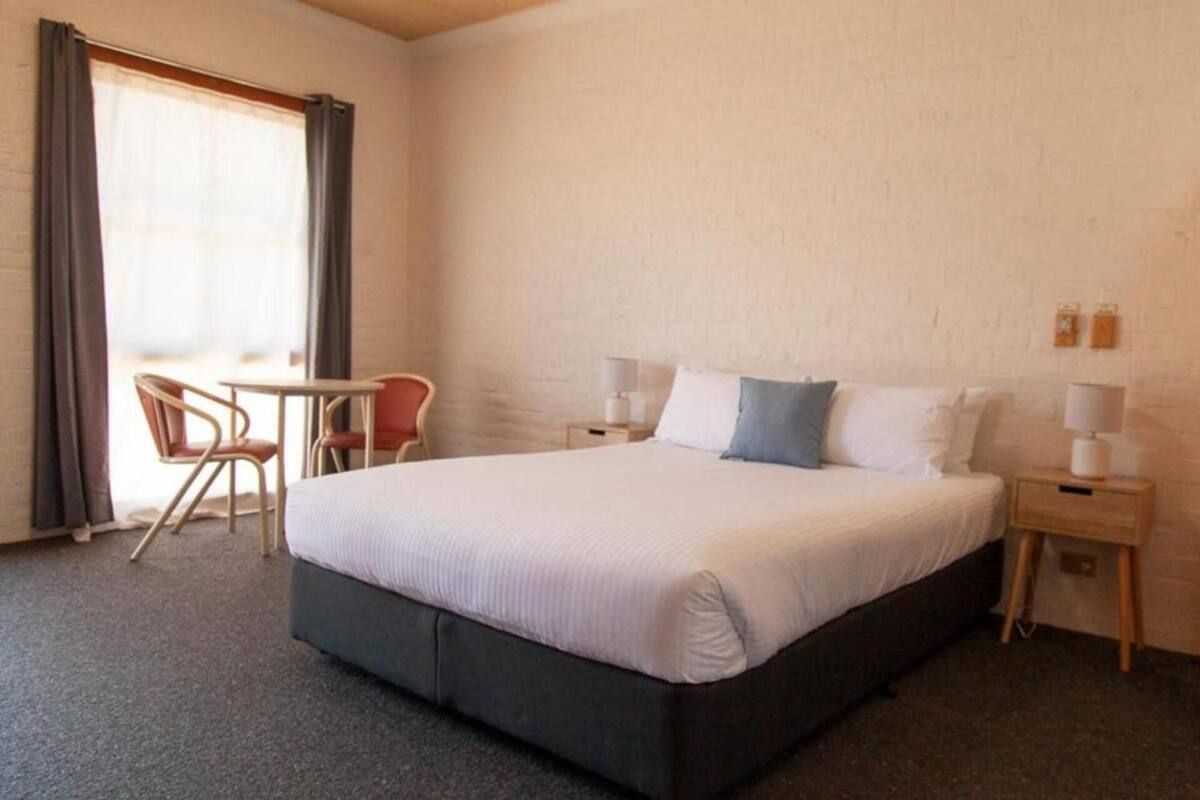 A hotel room with a large bed, a small table, two chairs, and a window with curtains.