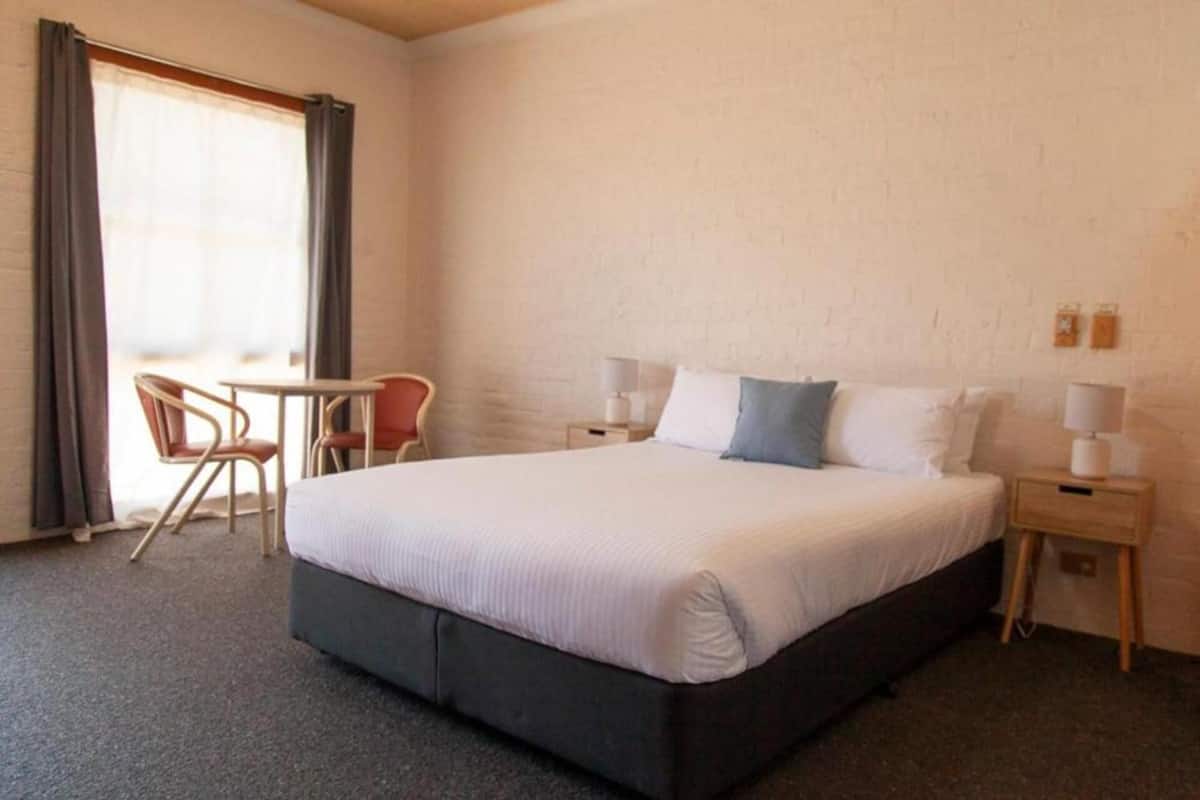 Hotellihuone, jossa on suuri sänky, pieni pöytä, kaksi tuolia ja ikkuna, jossa on verhot.