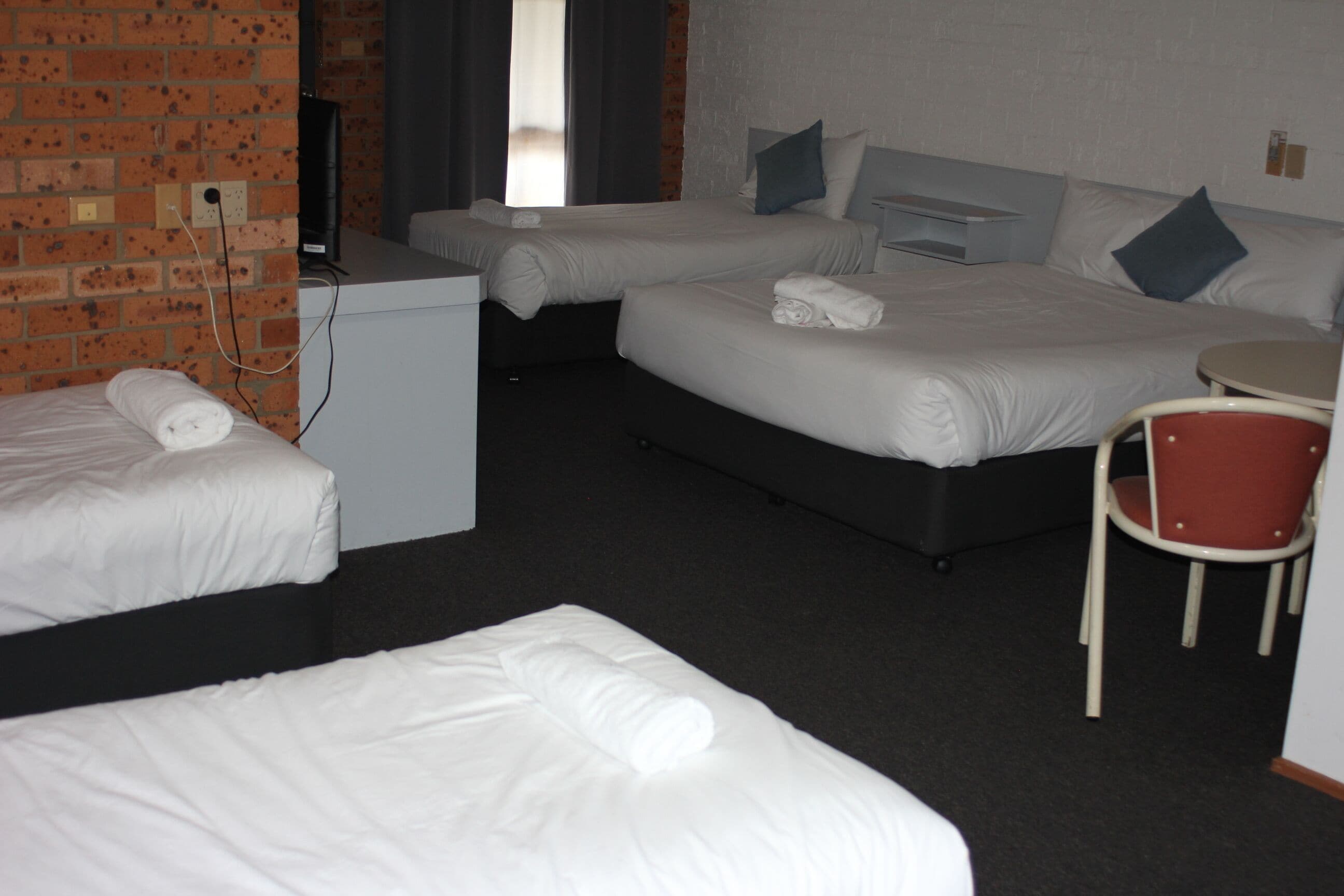 Habitación de hotel con dos camas individuales, una cama doble, un escritorio pequeño y una silla.