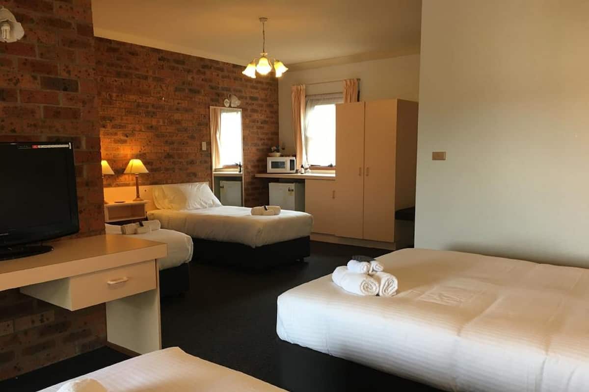 A hotel room with a brick wall, a television, two beds, a desk, and a wardrobe.